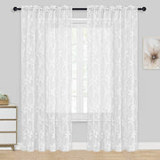White floral lace curtains hanging in a room with a small table and decorative item.